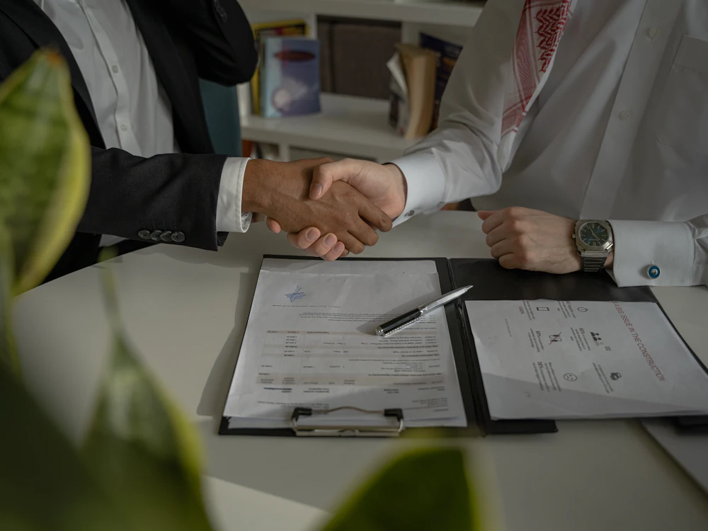Two business people shaking hands over signed paperwork after reaching an agreement
